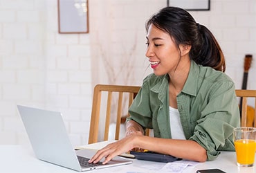 Young Hispanic woman at dining table working on laptop