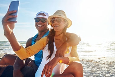 American couple on vacation taking selfie by the ocean.