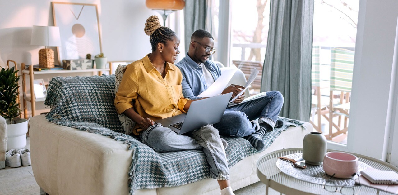 Smiling African-American couple reviewing documents on sofa with laptop