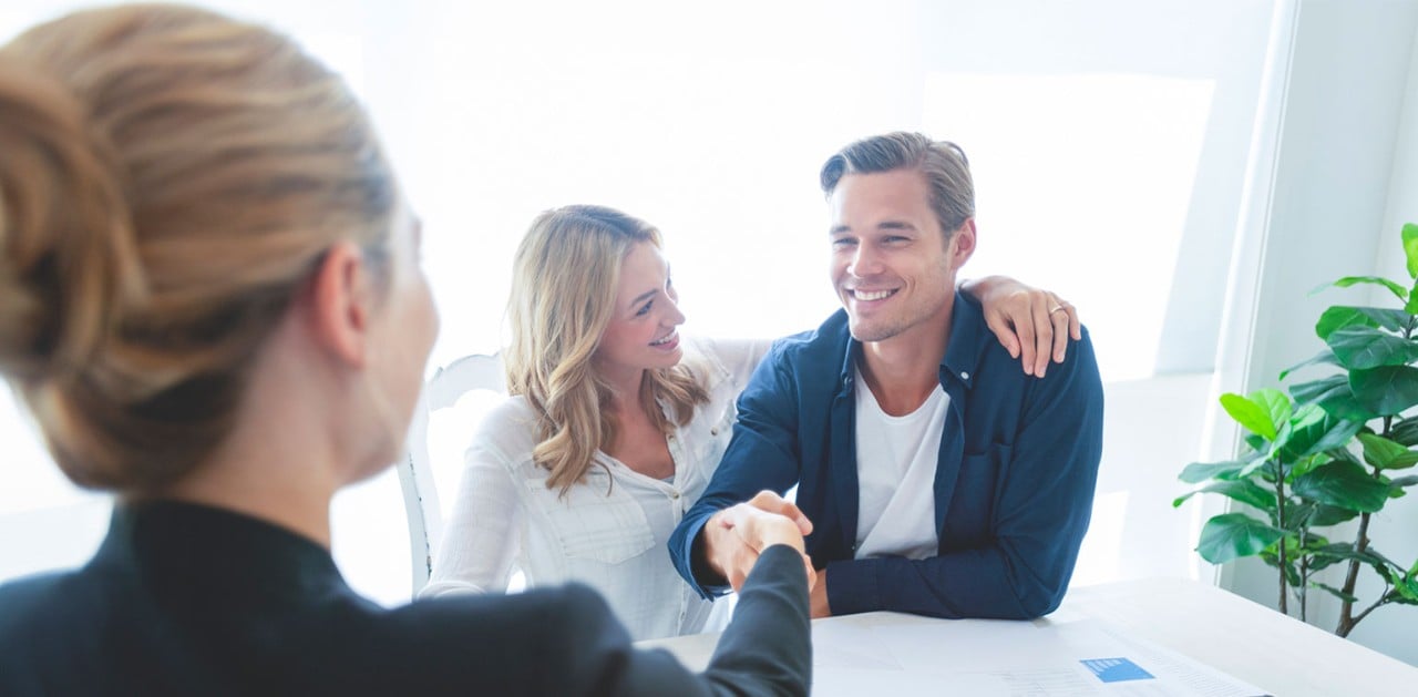 Smiling young Caucasian couple shaking hands with female banker