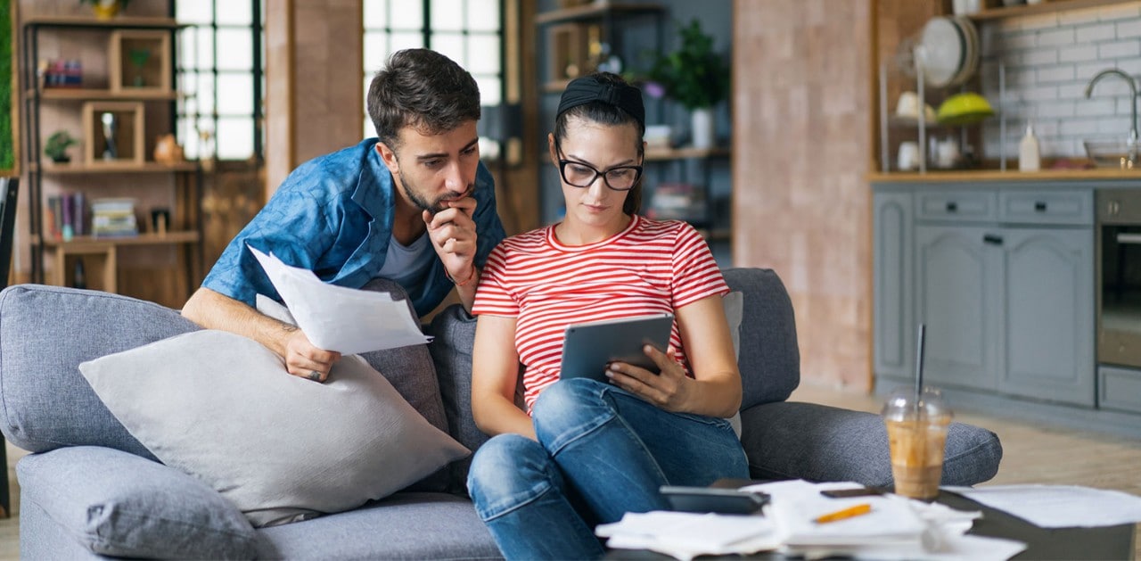 Young Caucasian couple reviewing documents on sofa with tablet