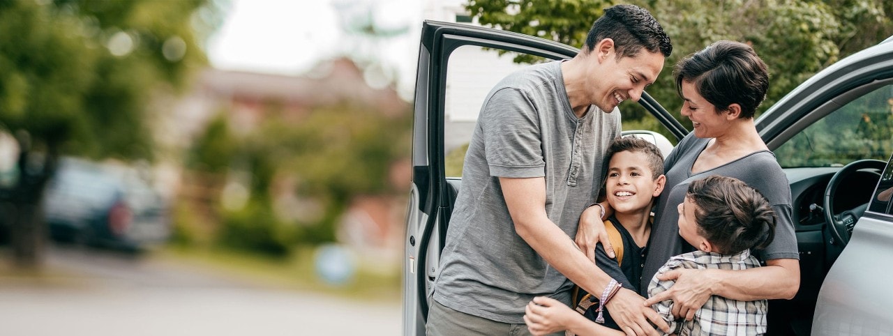 Hispanic parents hugging two young sons near a car