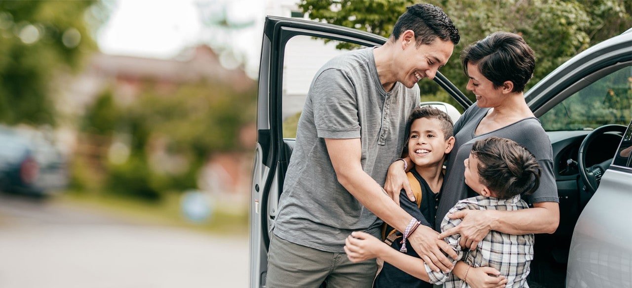Hispanic parents hugging two young sons near a car