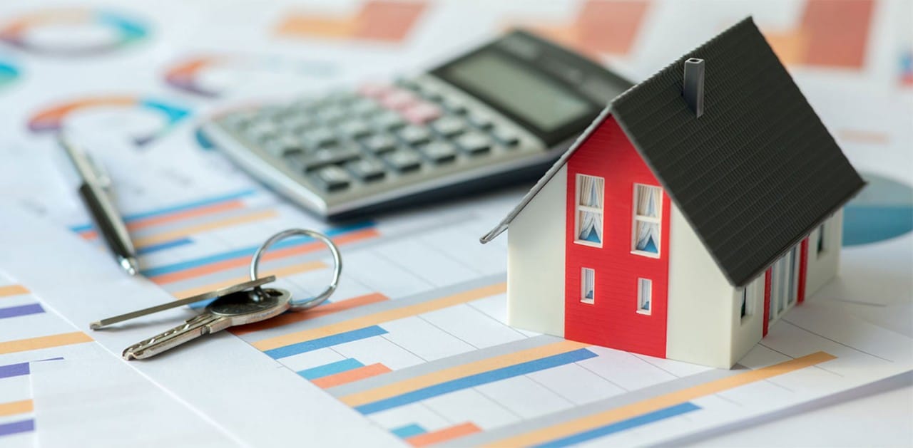 Small model of a house with keys, a pen, and a calculator, all on top of financial documents