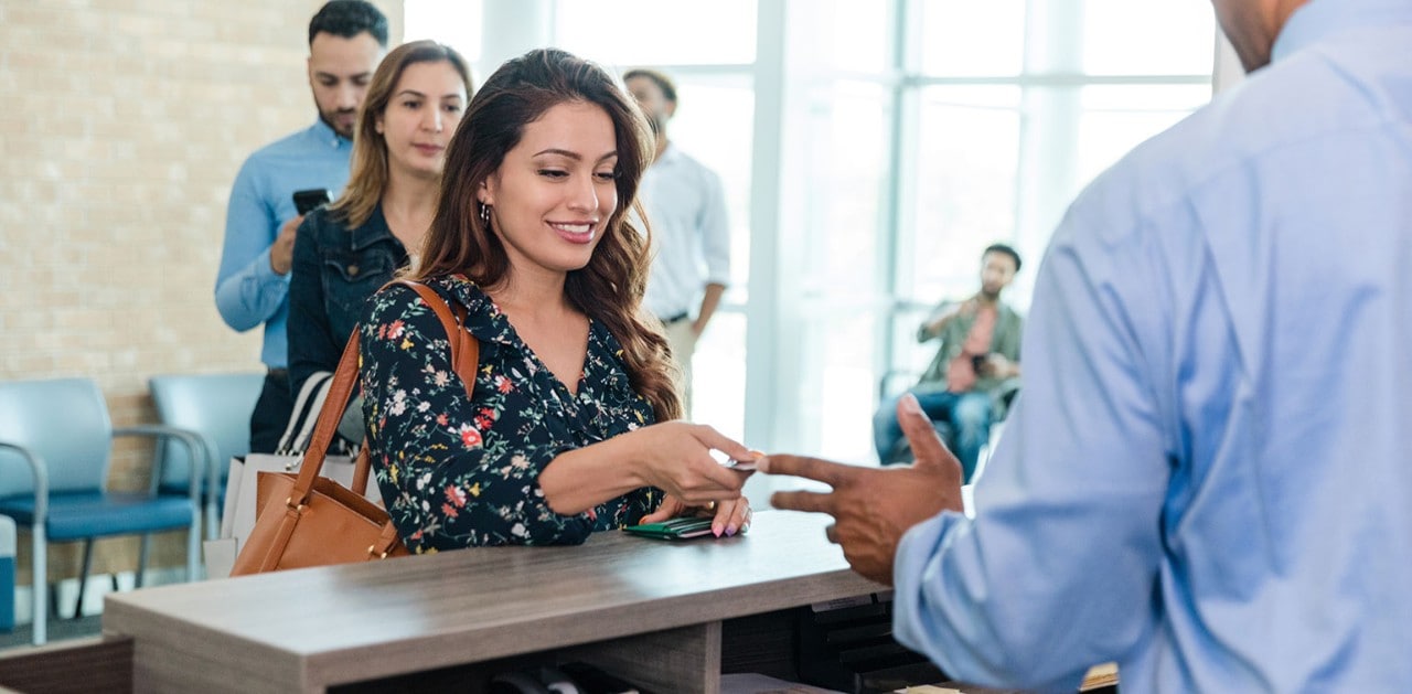 Young female bank client handing card to banker