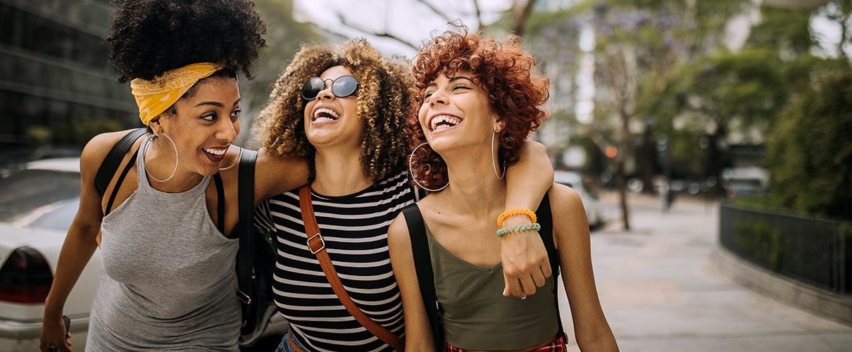 Diverse group of female friends embracing and laughing as they walk down the street.