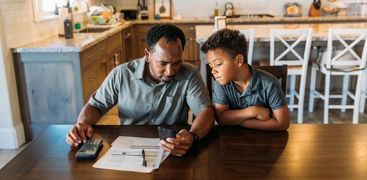 African-American father sitting at kitchen table teaching his young son about finances