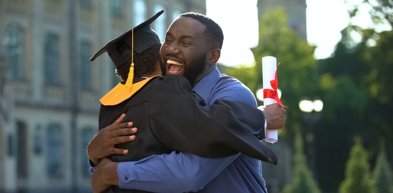 African-American father hugging graduating son holding diploma