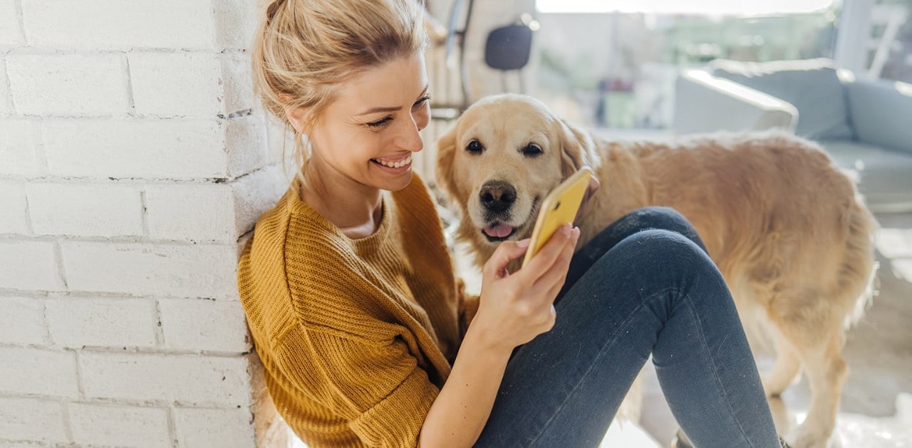 Woman sitting on floor taking quiz on smartphone with dog looking on