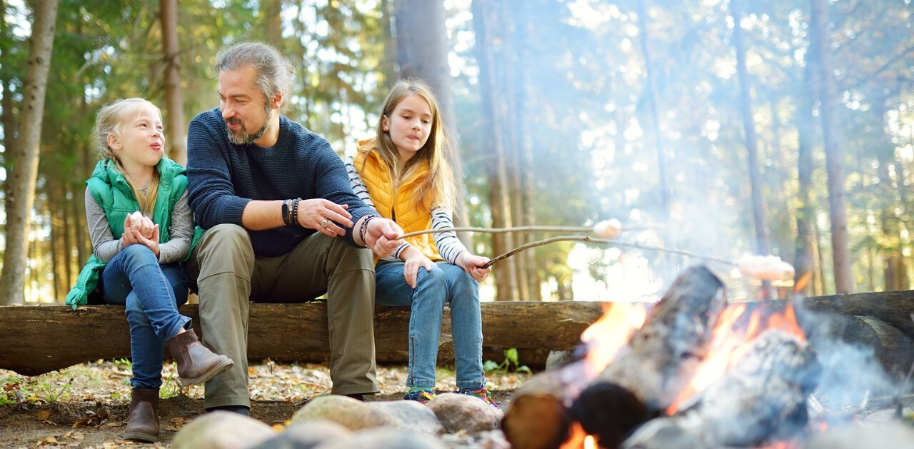 Father with two young daughters roasting marshmallows over campfire