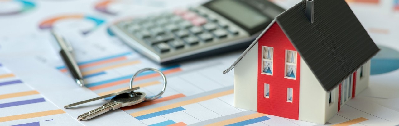 Small model of a house with keys, a pen, and a calculator, all on top of financial documents