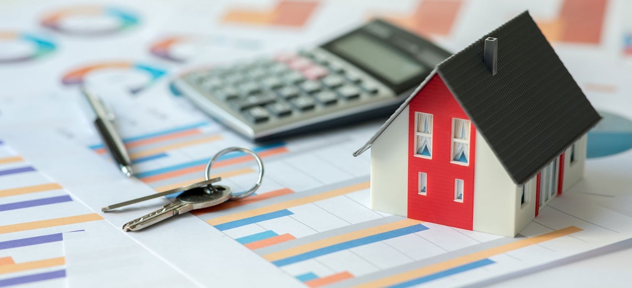 Small model of a house with keys, a pen, and a calculator, all on top of financial documents
