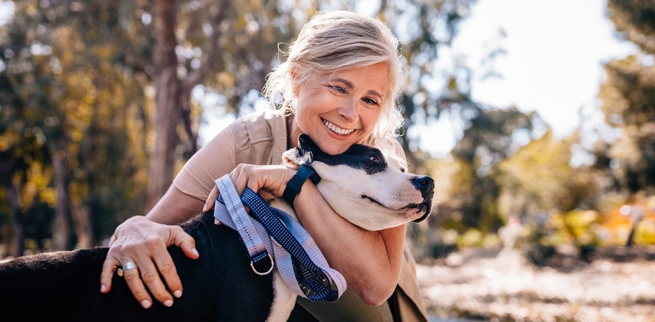 Happy senior woman enjoying walk in nature and embracing pet dog in forest park