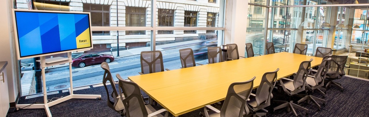 A board room with empty seats and a tv screen for projecting.