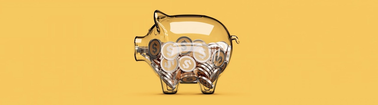 lear piggy bank full of coins in front of yellow background.