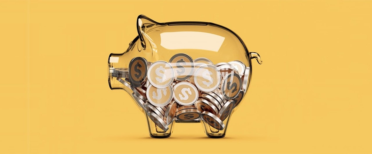 Clear piggy bank full of coins in front of yellow background.