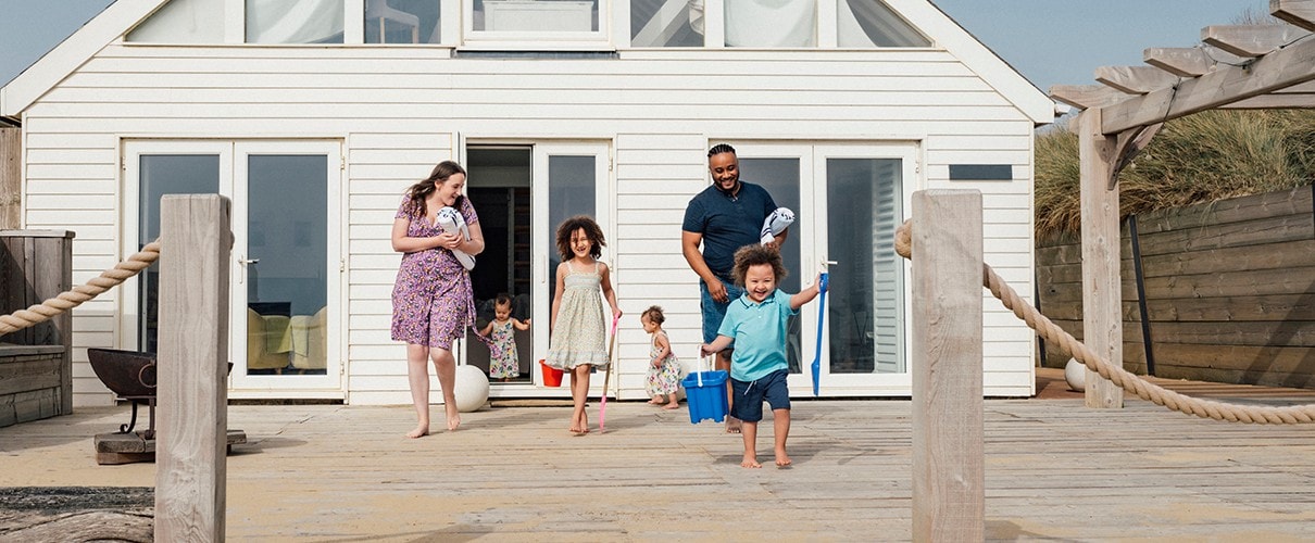 Multiracial parents and their children walking across vacation home deck toward the beach