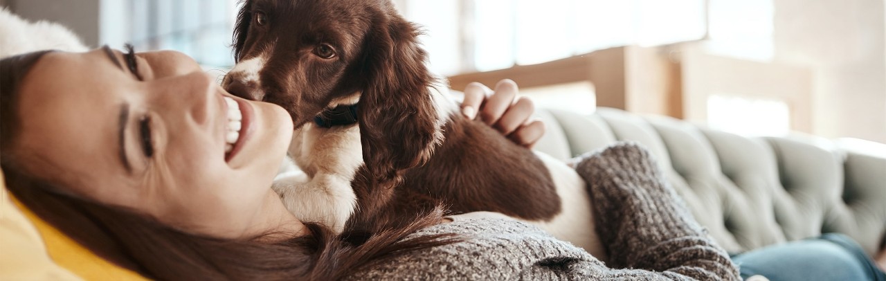 Puppy licking woman’s cheek while laying on couch