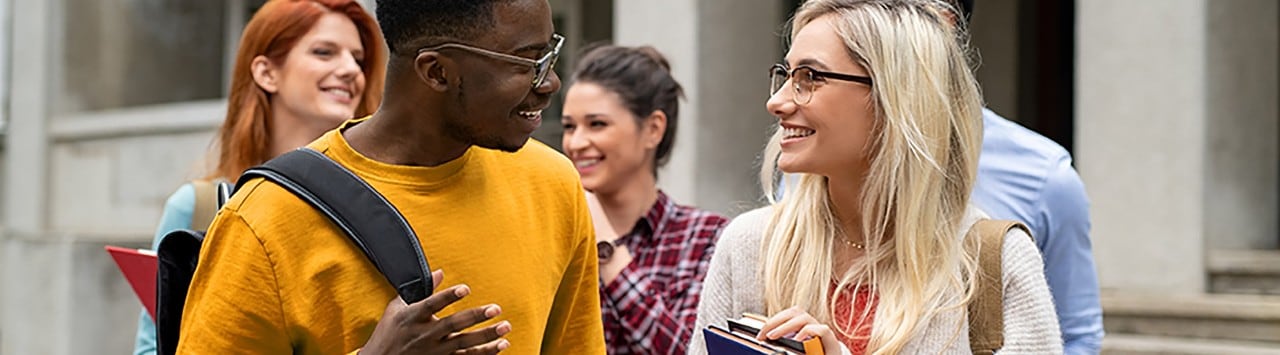 Diverse students carrying books and having conversation outside college building