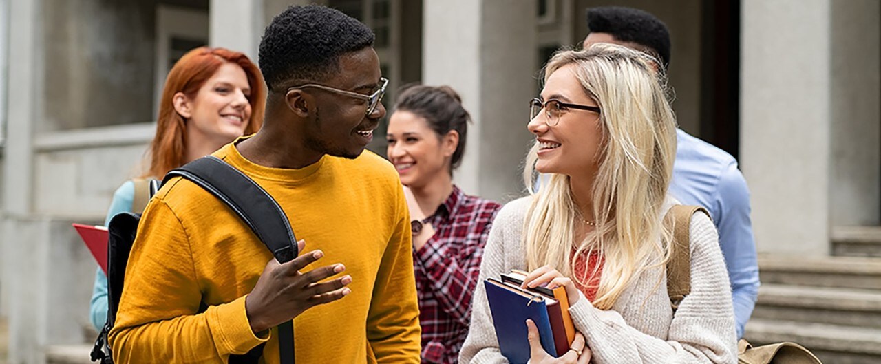 Diverse students carrying books and having conversation outside college building