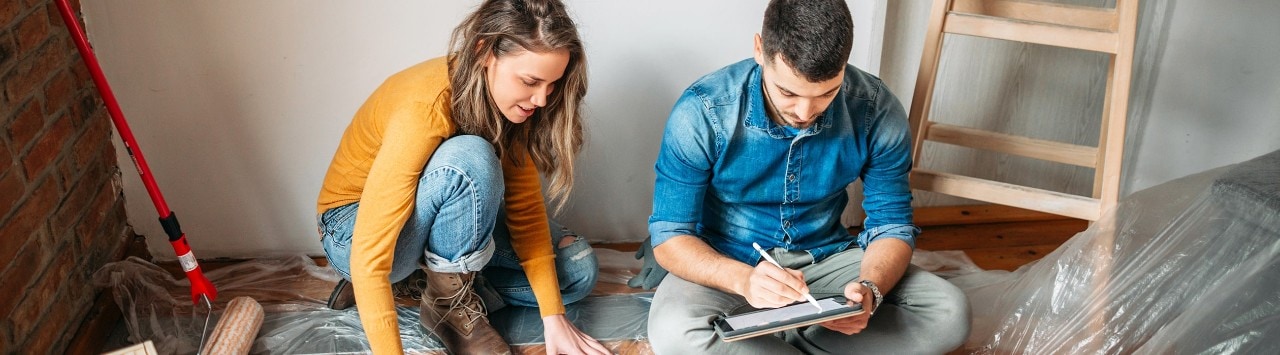 Young couple sitting on floor during home renovation looking at blueprint and table