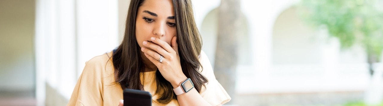 Young woman holding her hand over mouth looking at her smartphone with a shocked look