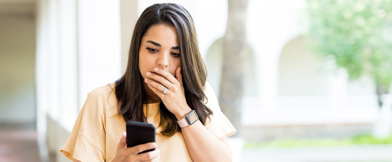 Young woman holding her hand over mouth looking at her smartphone with a shocked look