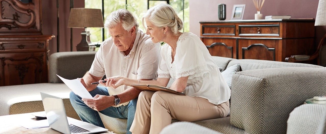 Senior couple reviewing financial documents with laptop