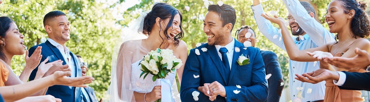 Happy married couple walking down the aisle while guests throw rose petals