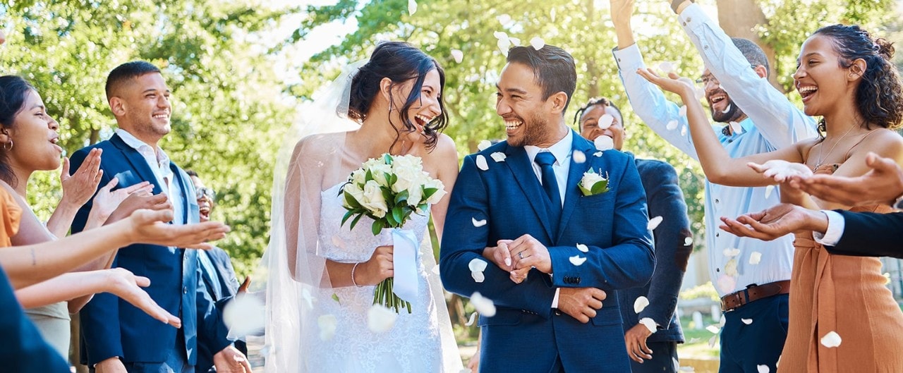 Happy married couple walking down the aisle while guests throw rose petals