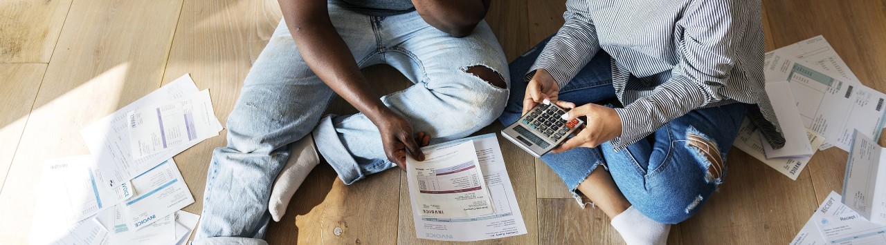 Couple sitting on floor reviewing bills and calculating debt