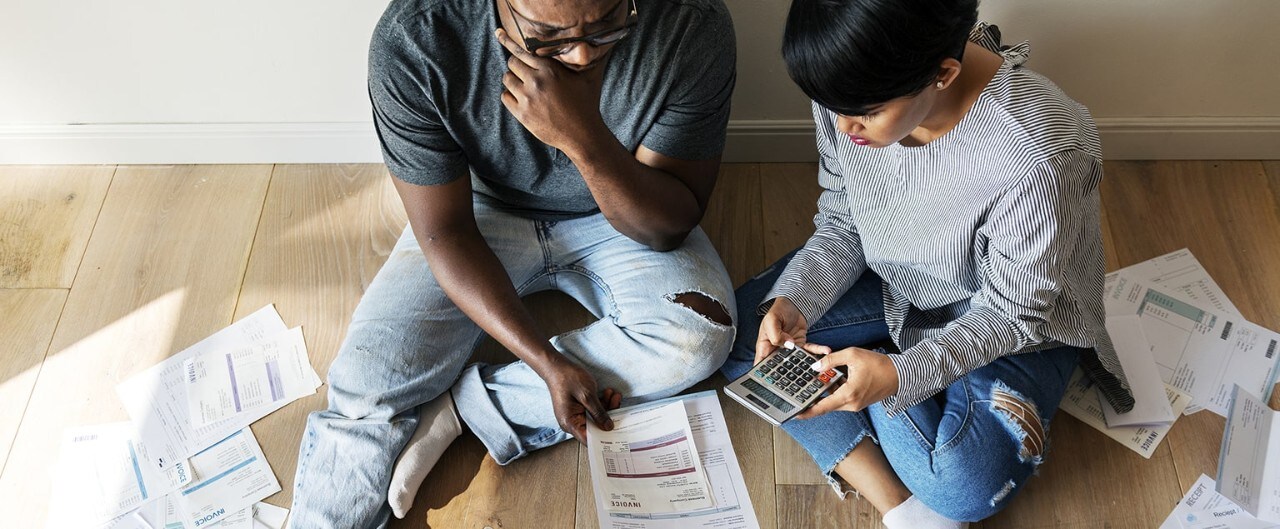 Couple sitting on floor reviewing bills and calculating debt