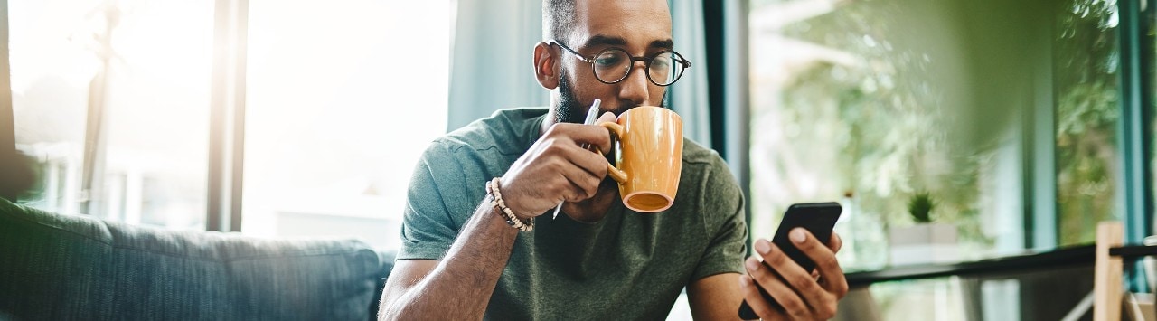 African-American man sipping coffee and looking at smartphone
