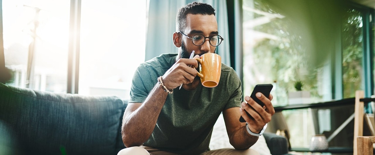 African-American man sipping coffee and looking at smartphone