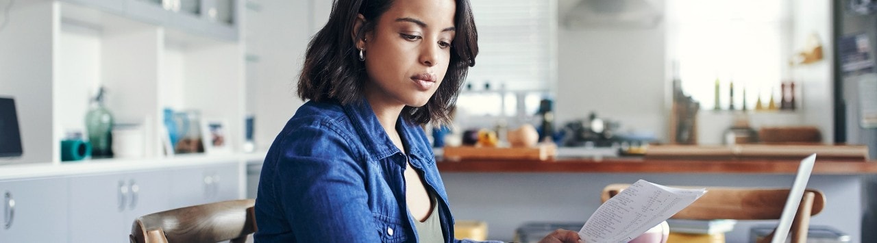 Shot of a young woman using a laptop and  going through paperwork while working from home