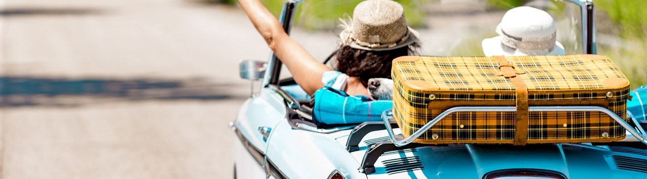 Women in vintage convertible with suitcase on trunk rack