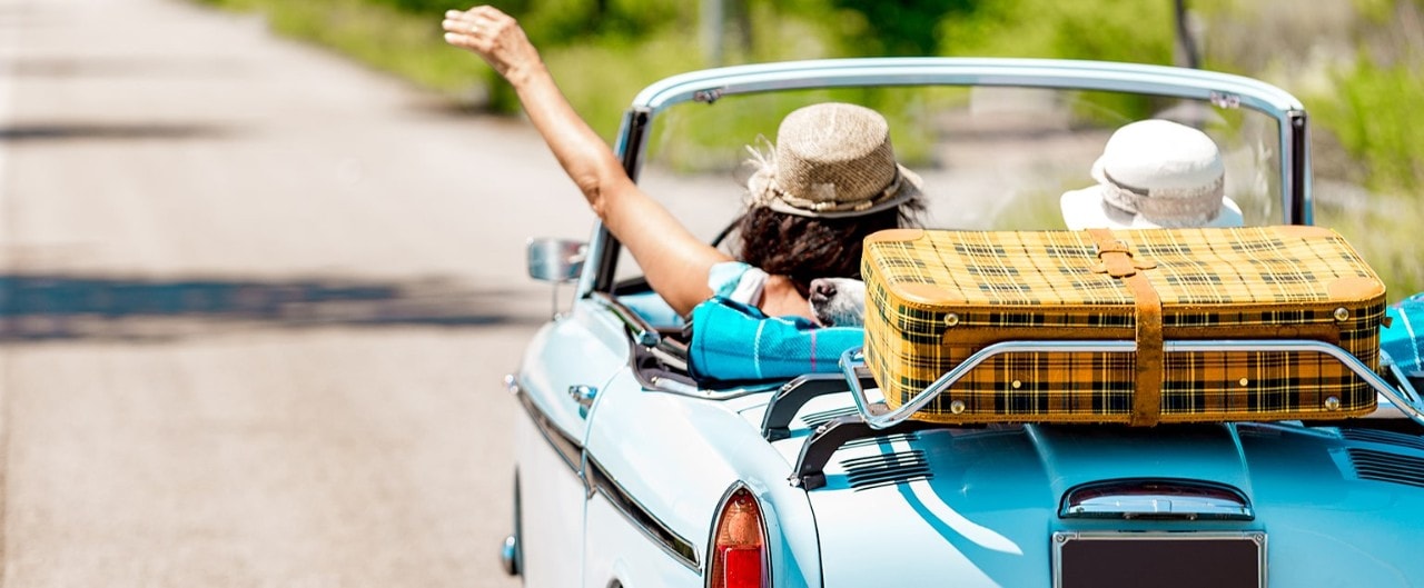 Women in vintage convertible with suitcase on trunk rack