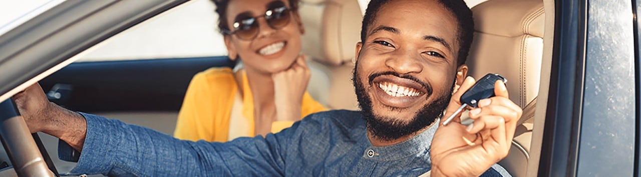 Happy African-American couple sitting in new car holding keys