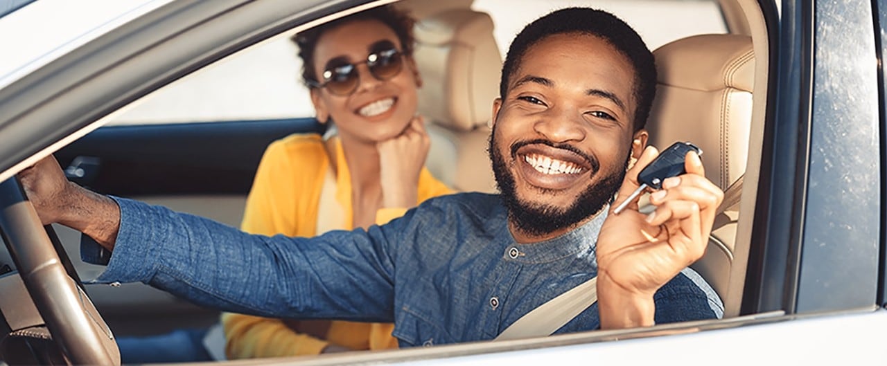 Happy African-American couple sitting in new car holding keys