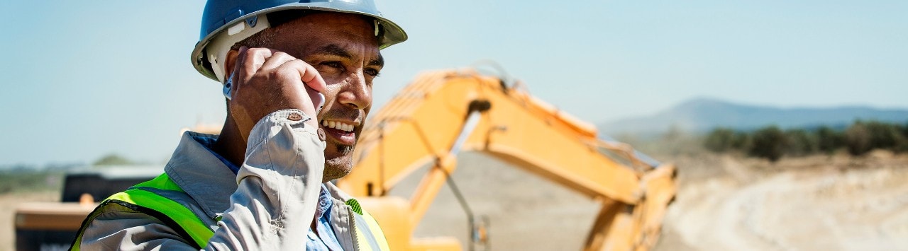 Hispanic construction foreman on phone with bulldozer in background