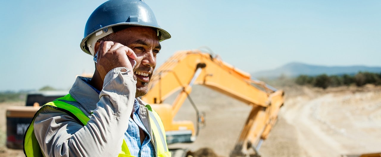 Hispanic construction foreman on phone with bulldozer in background