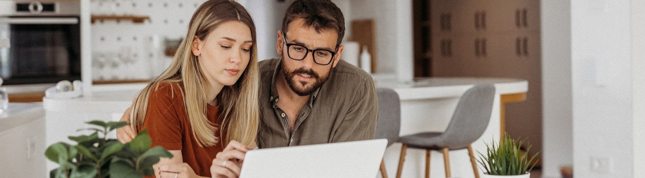 Couple at kitchen table paying bills on laptop