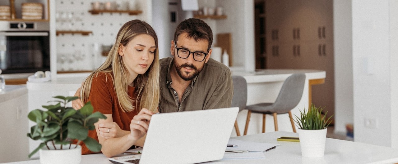 Couple at kitchen table paying bills on laptop