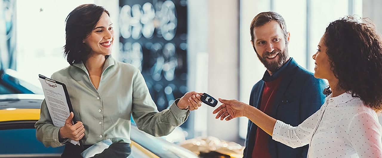 Car saleswoman handing keys to multiracial couple