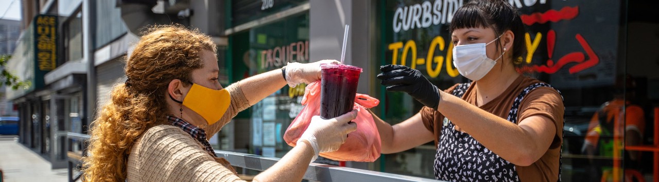 Masked restaurant employee hands order to customer at curbside pick-up