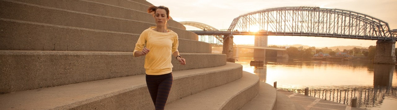 Woman running on steps of Serpentine Wall with Ohio River and bridge in background