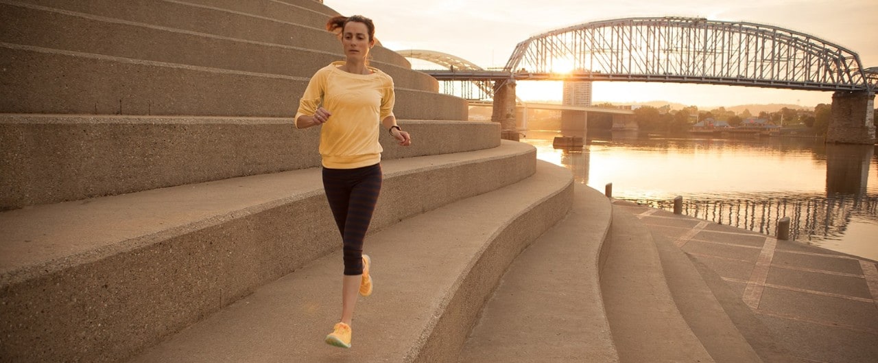 Woman running on steps of Serpentine Wall with Ohio River and bridge in background