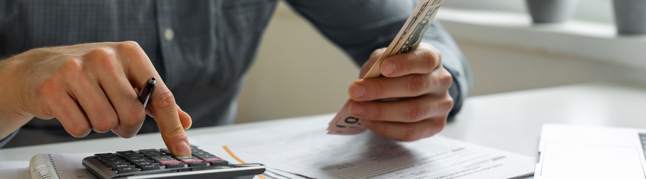 Man holding cash and using calculator to pay bills