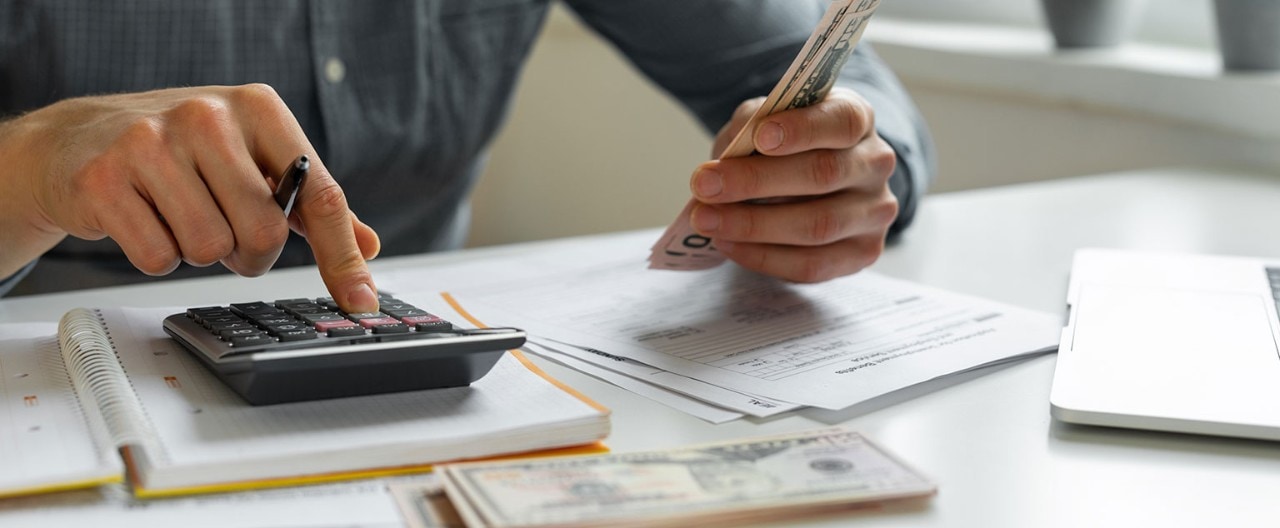 Man holding cash and using calculator to pay bills