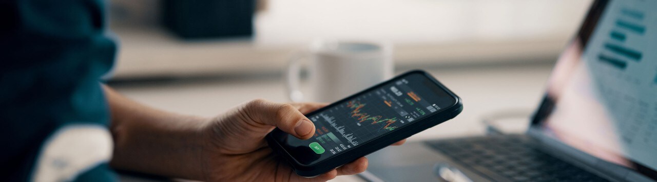 Man reviewing financial data on smartphone and laptop